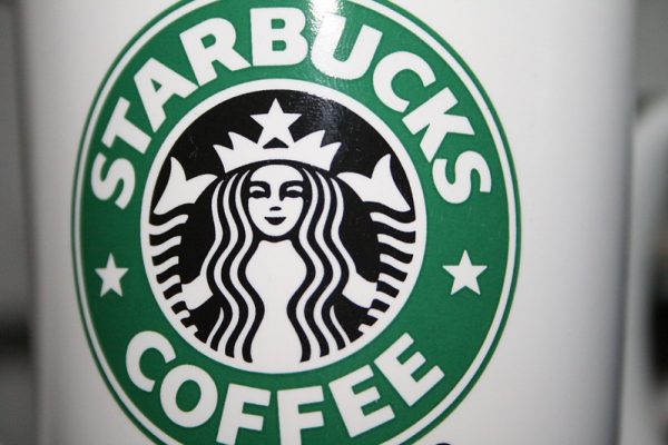 A closeup shot of a white coffee mug with the green and black Starbucks logo on it
